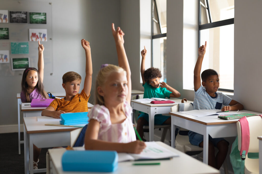 Students actively participating in class by raising their hands, representing a supportive learning environment that encourages parents to stop forcing kids to be doctors or engineers.
