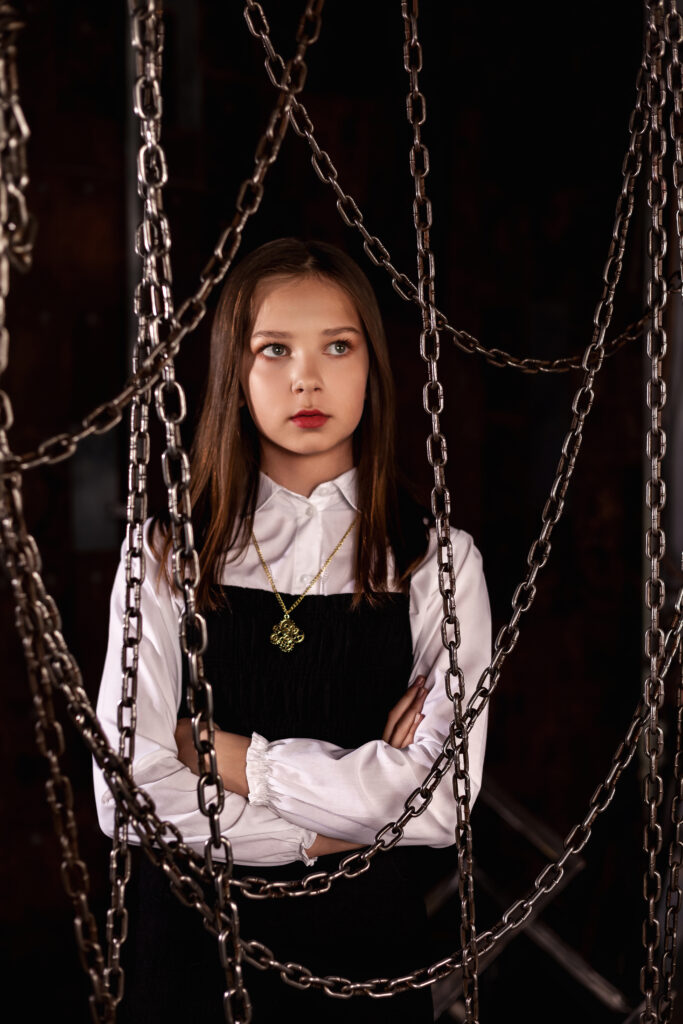 A young girl standing behind chains, symbolizing the restrictions children face when parents stop forcing kids to be doctors or engineers.