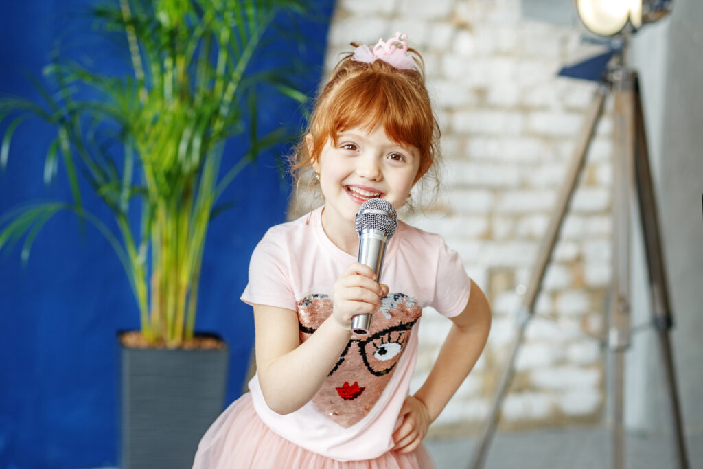 How to speak English confidently – a small girl speaking confidently into a microphone, smiling while addressing an audience.