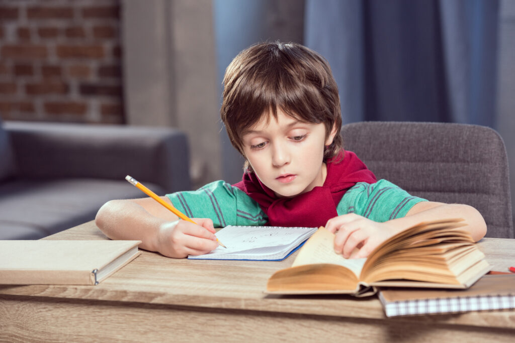 How to learn English – boy reading and writing in a notebook while studying attentively.