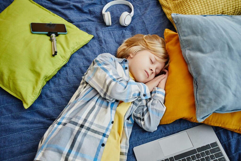 Child sleeping peacefully with headphones and laptop aside, showing the importance of healthy sleep habits and managing screen time for children.
