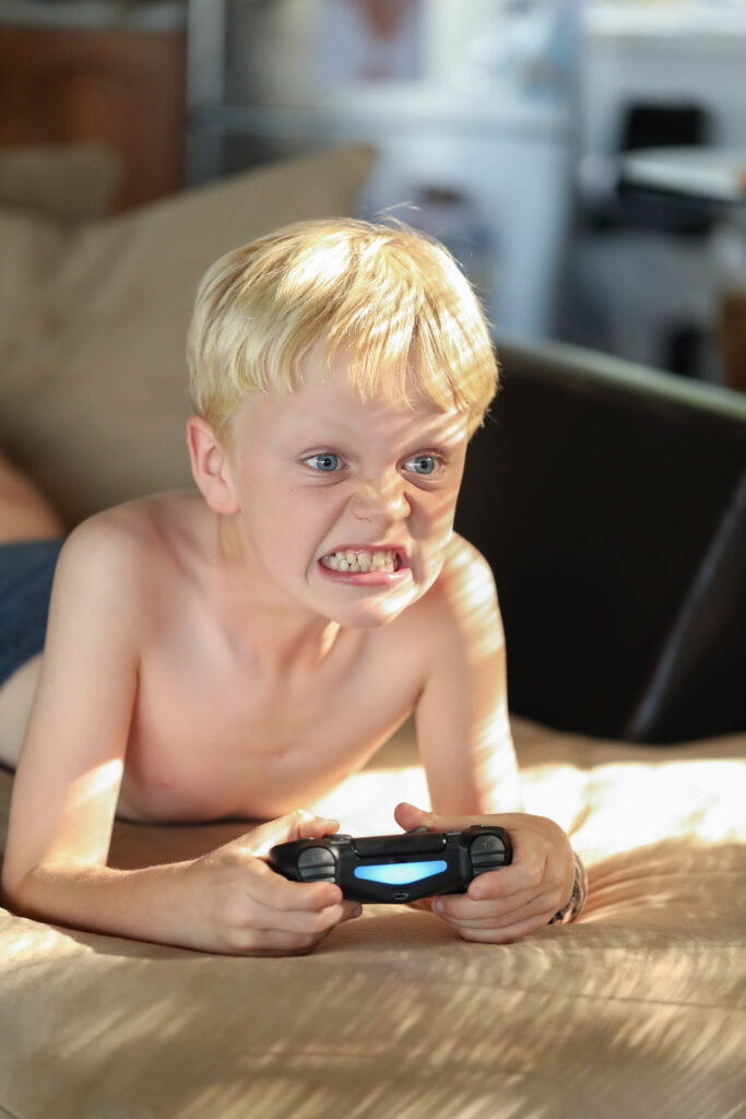 A boy playing a dangerous video game with a frustrated face, showing the negative effects of harmful online games on children’s mental health and behavior.