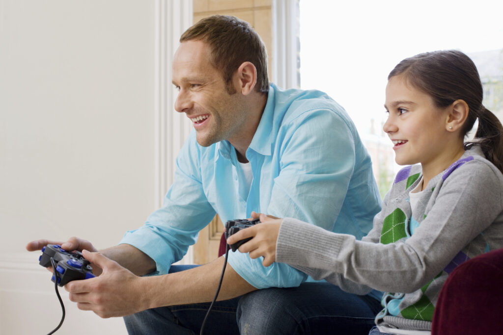 Father playing video games with child instead of encouraging outdoor play, highlighting the impact of excessive screen time on children’s health and habits.