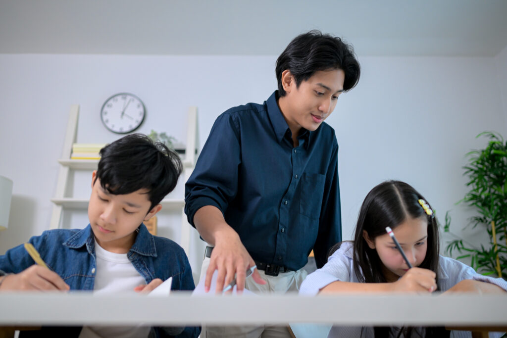 How to learn English – father teaching his two kids at home with books and notebooks, helping them study together.