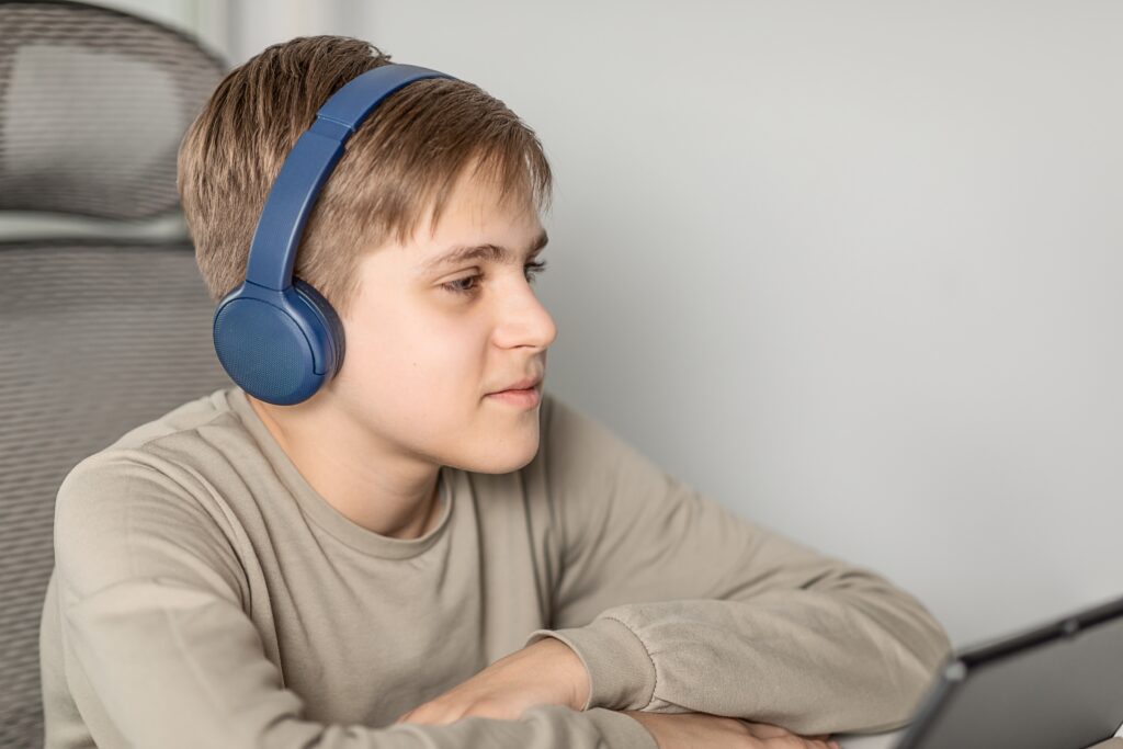 A boy wearing headphones and listening to audio lessons to learn English effectively.