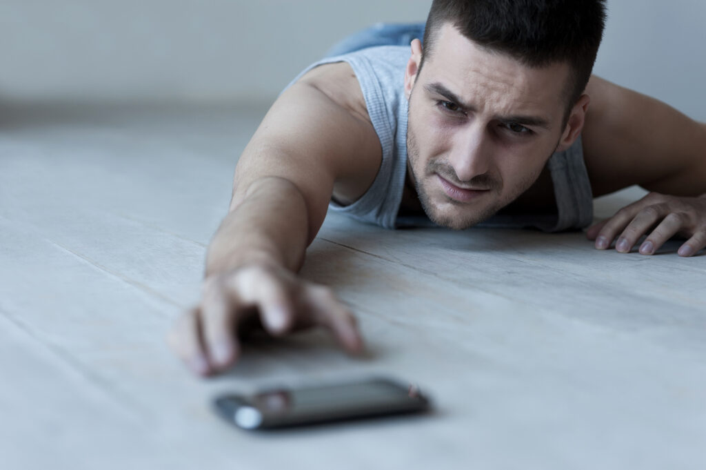 A man crawling on the ground, desperately reaching for a smartphone, symbolizing the extreme phone addiction effects and dependency.