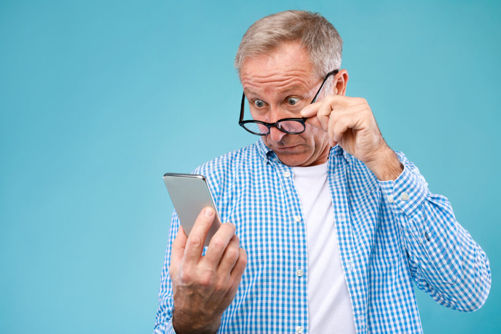 A senior man squinting at his smartphone screen, illustrating challenges and signs of digital addiction.